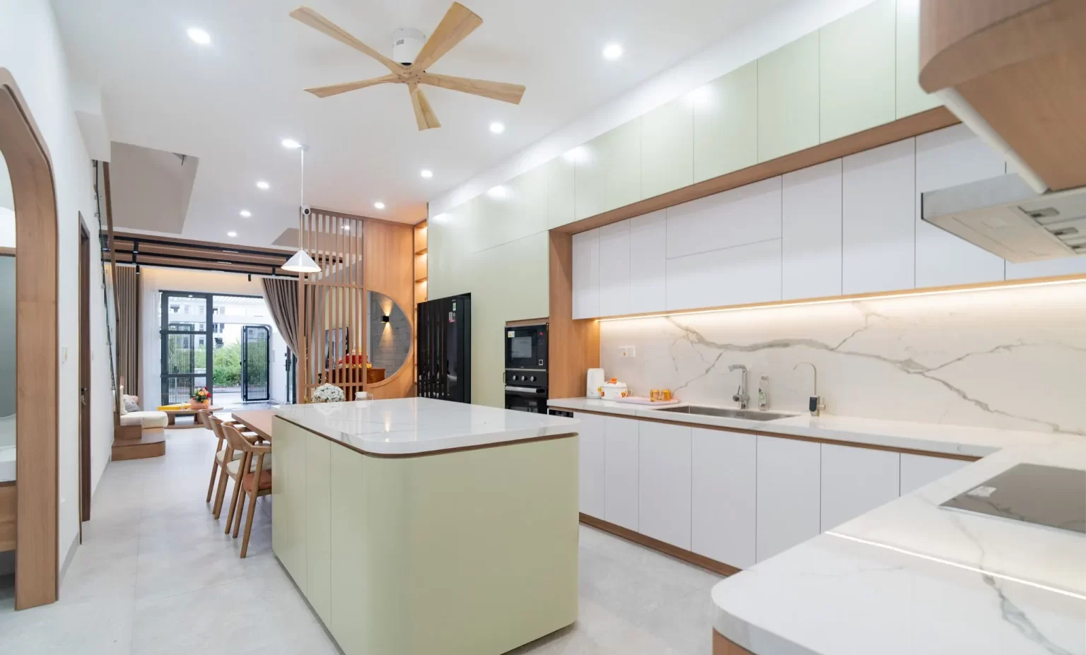Phòng bếp được bố trí thêm đảo bếp cạnh bàn ăn, giúp tăng tiện ích. Không gian sang trọng với tone màu trắng – nâu – xanh chủ đạo, mang cảm giác tươi mới. Mặt và vách khu vực bếp nấu ốp đá trắng vân mây, tăng thêm điểm nhấn thẩm mỹ cho căn bếp
